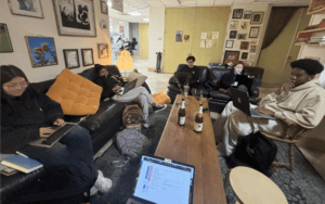 A photo of five people sitting in a circle on couches on their laptops